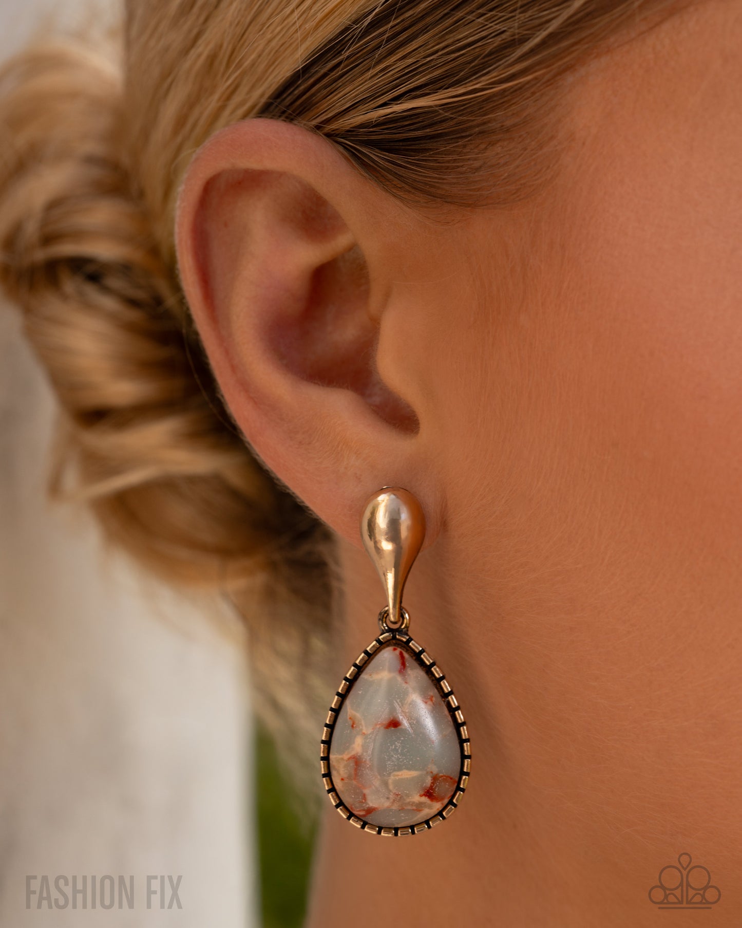 Teardrop-shaped earring worn by a person with blonde hair, against a neutral background.
