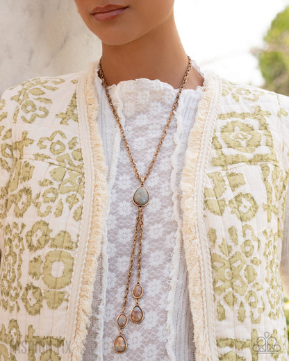 Person wearing a long necklace with a detailed vest and white shirt.