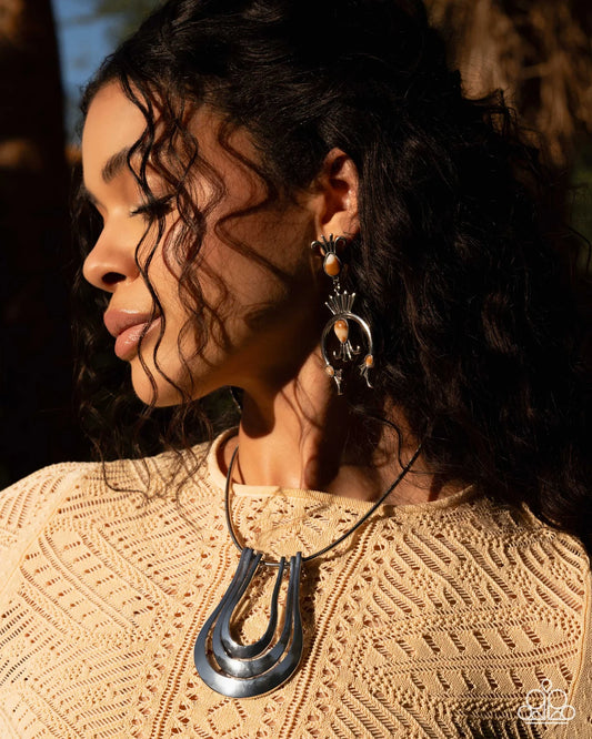 Woman wearing large earrings and a necklace with a textured beige top.