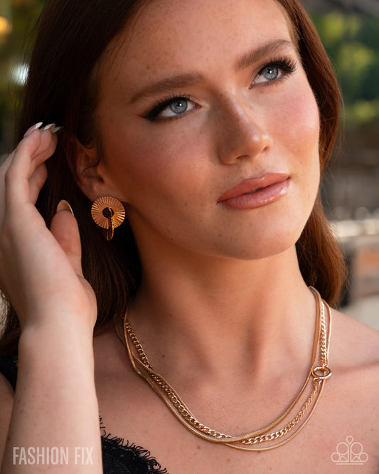 Woman wearing gold earrings and necklaces with a blurred outdoor background