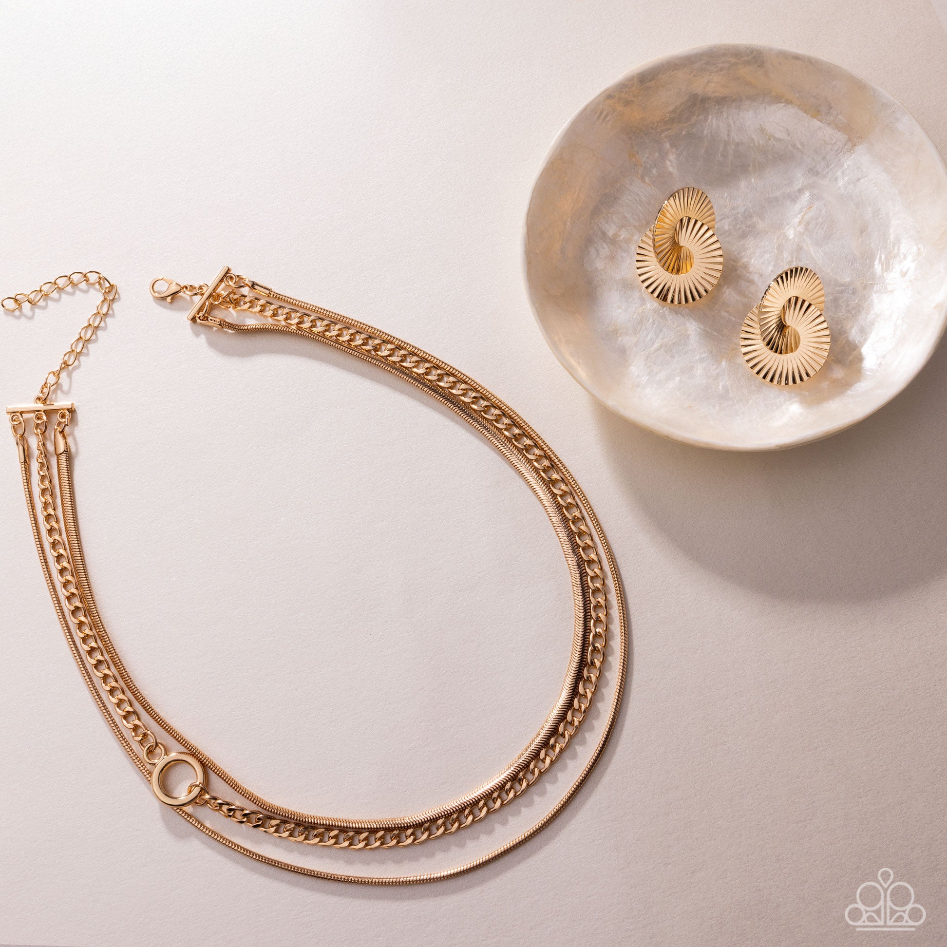 Gold chain necklace and earrings on a light surface with a decorative stone.