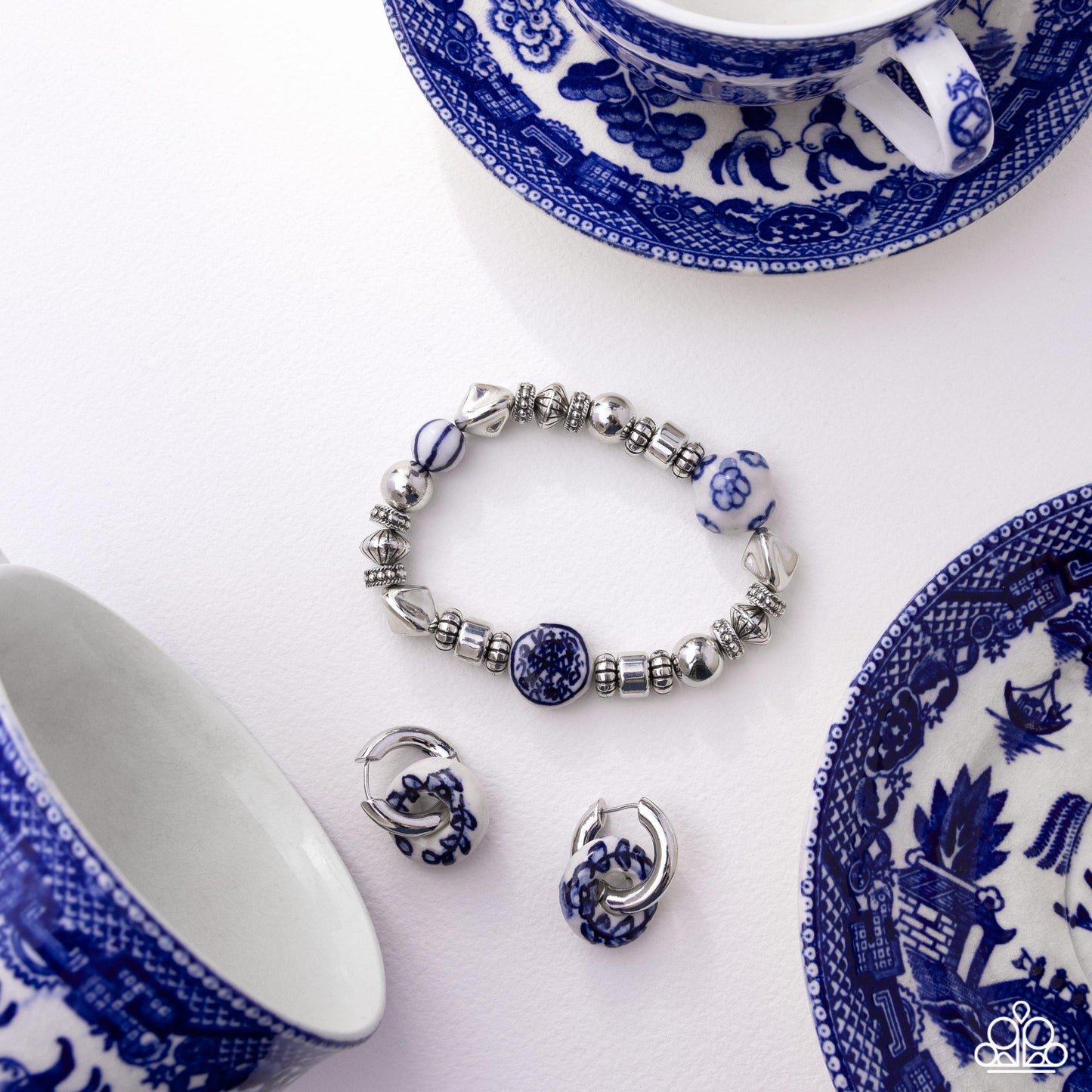 Jewelry set with bracelet and earrings on a white background with blue and white patterned teacups and saucers.