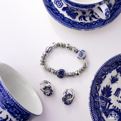 Jewelry set with bracelet and earrings on a white background with blue and white patterned teacups and saucers.