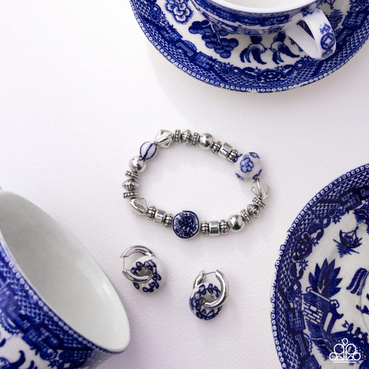 Jewelry set with bracelet and earrings on a white background with blue and white patterned teacups and saucers.