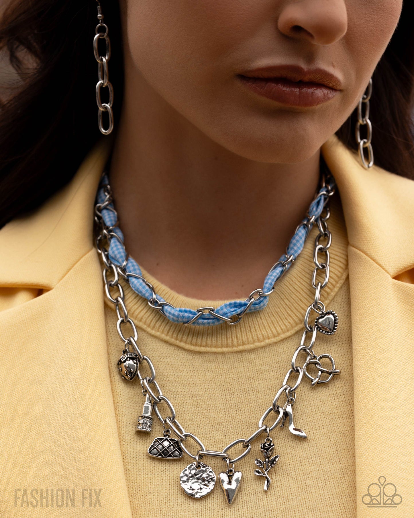 Close-up of a person wearing a silver charm necklace with a blue braided cord, set against a neutral background.