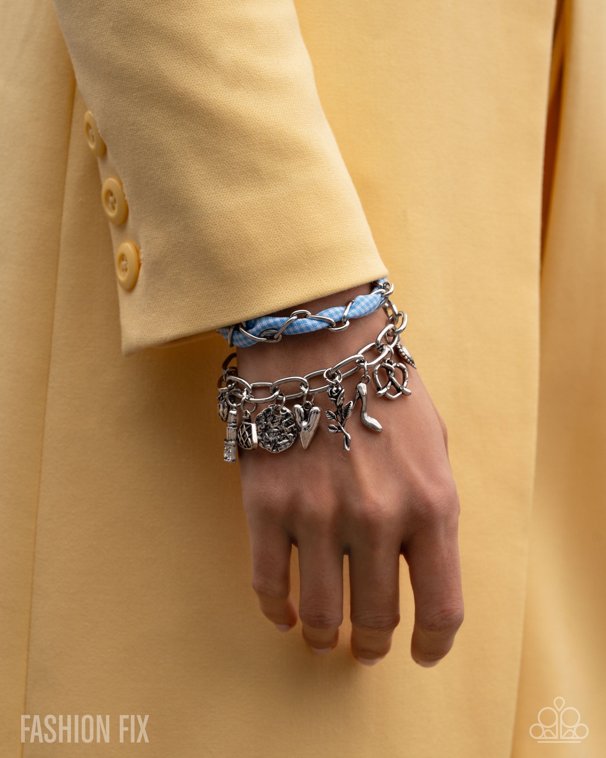 Hand wearing a silver charm bracelet with a yellow coat in the background