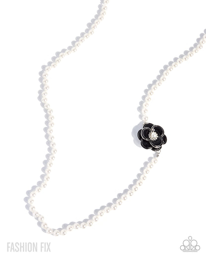 A white pearl necklace with a black flower-shaped charm featuring a clear crystal center, displayed on a clean white background with soft shadows.