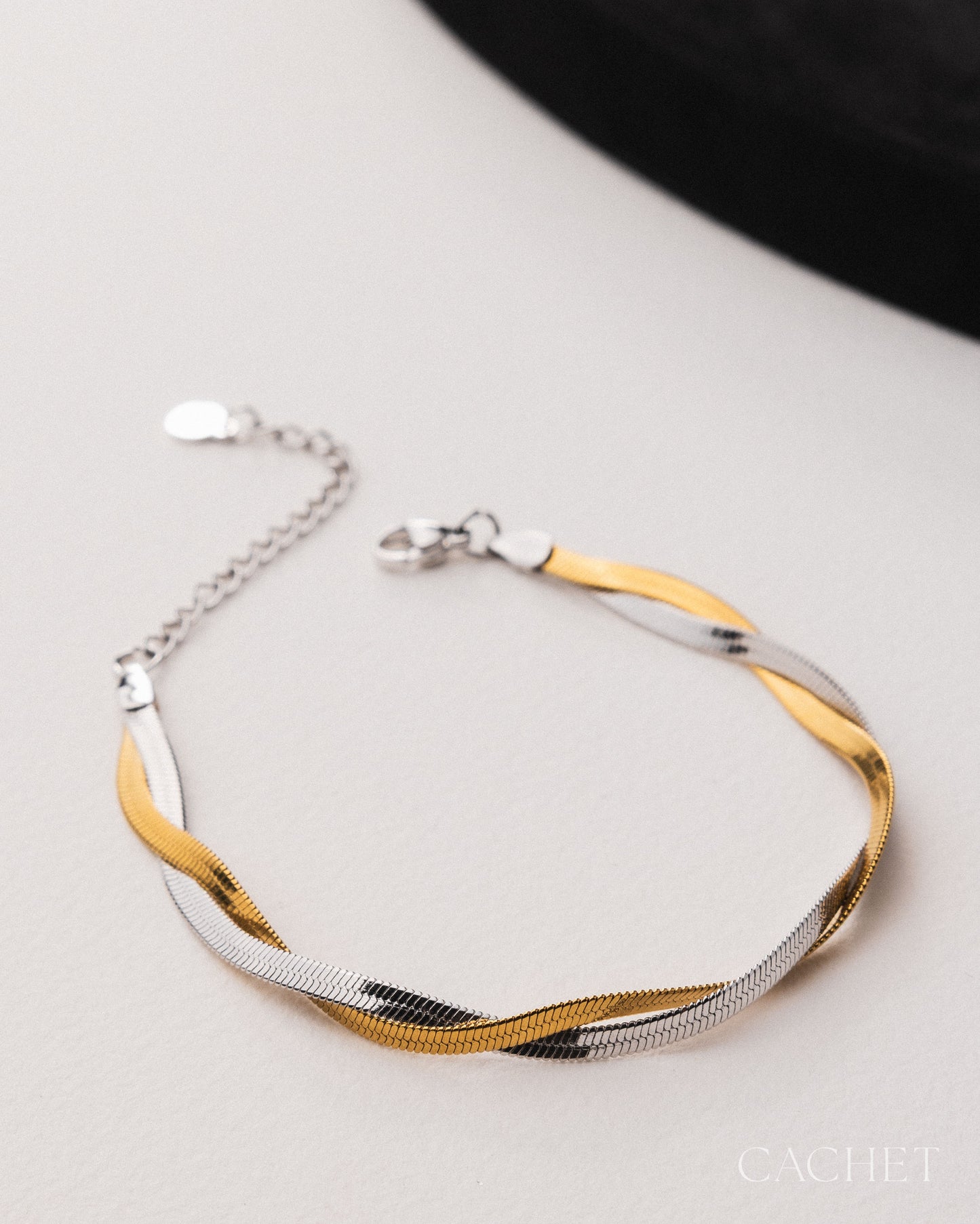 Two-toned gold and silver bracelet on a light gray surface with 'Cachet' branding.