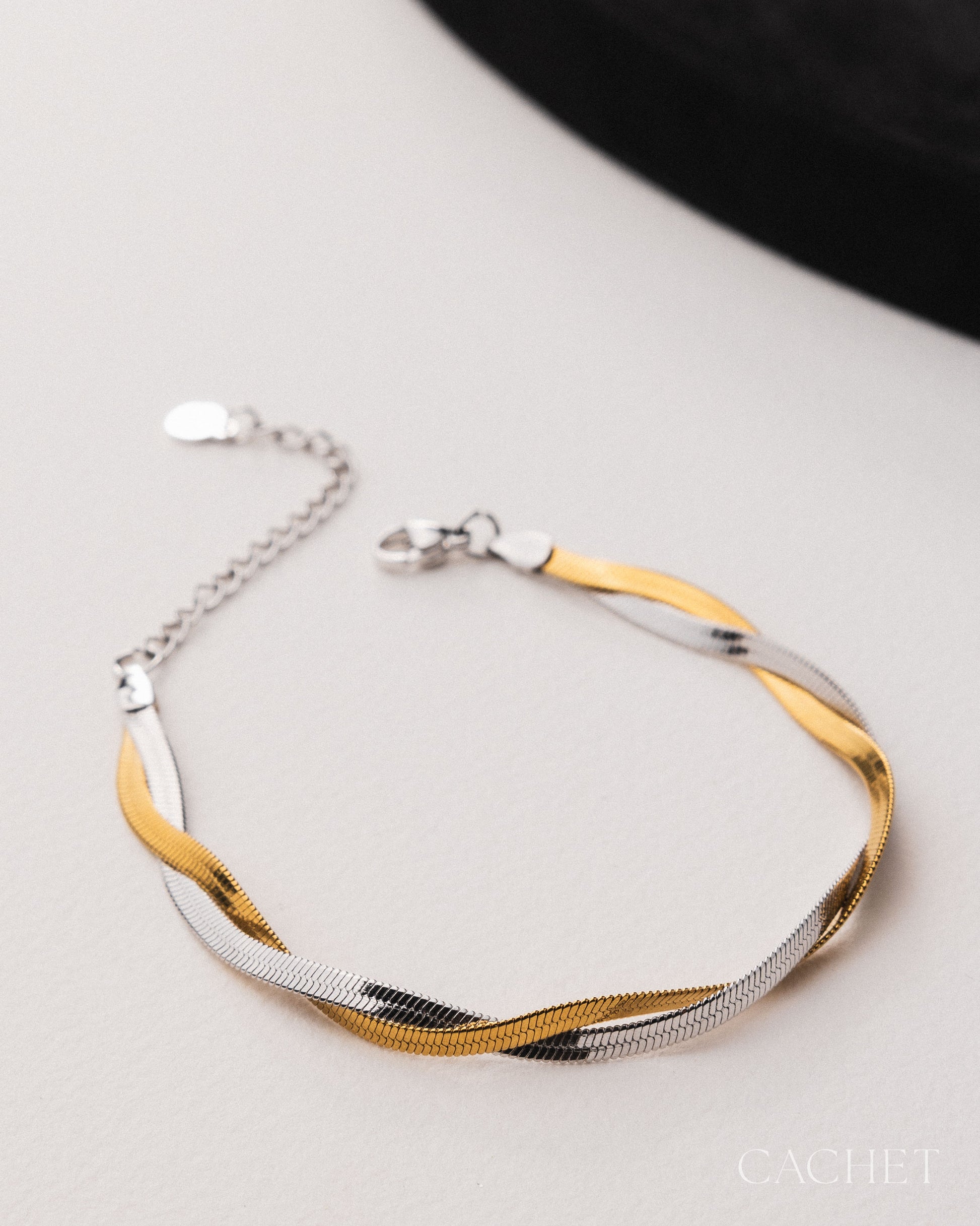 Two-toned gold and silver bracelet on a light gray surface with 'Cachet' branding.
