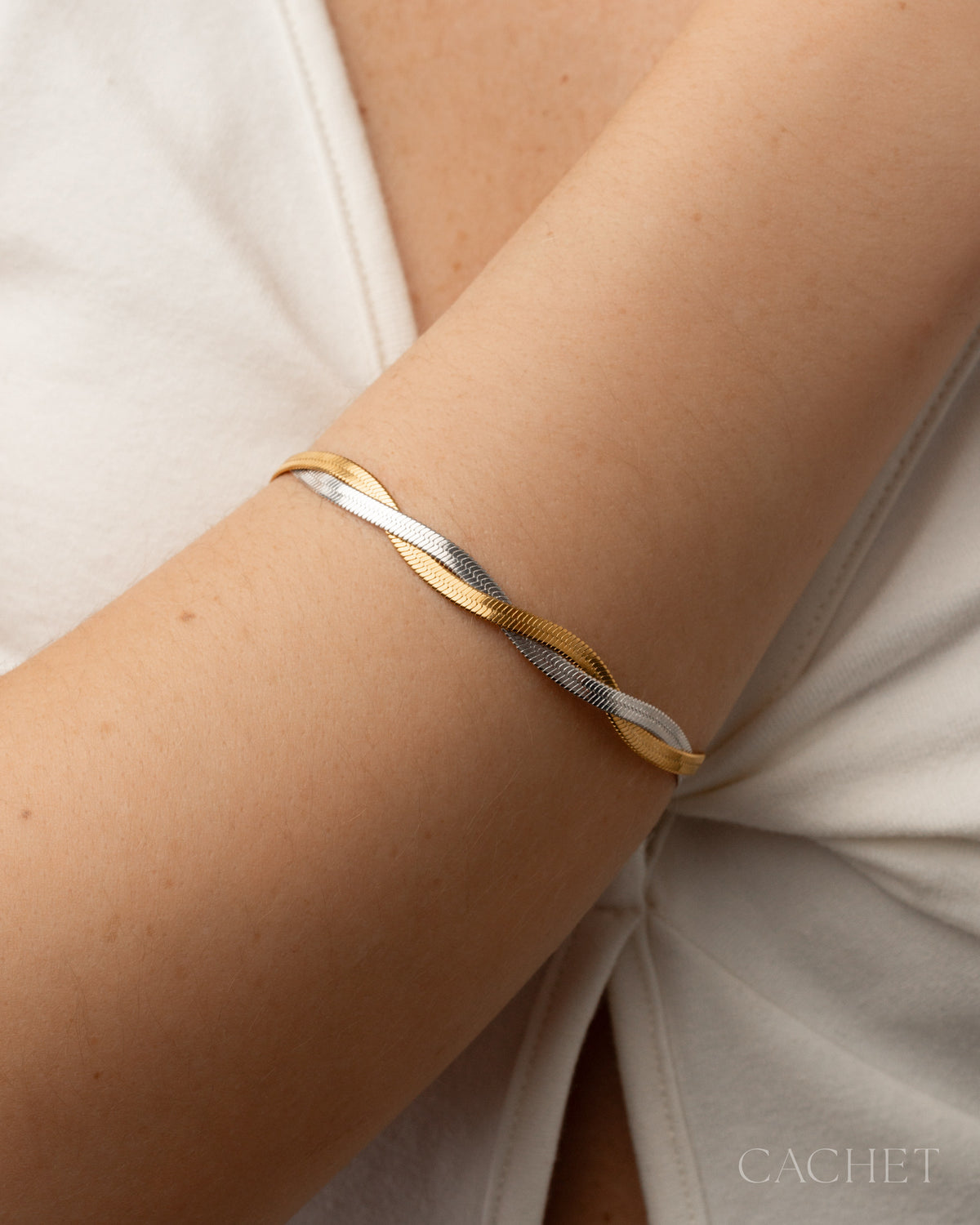 Two-toned gold and silver bracelet on a person's wrist with a light background.