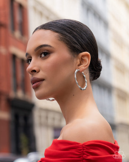 Woman wearing large hoop earrings with a blurred city street background