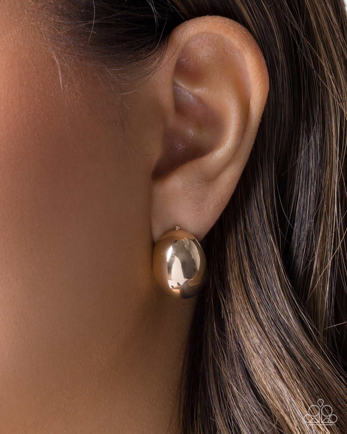Gold hoop earring worn by a person with brown hair.
