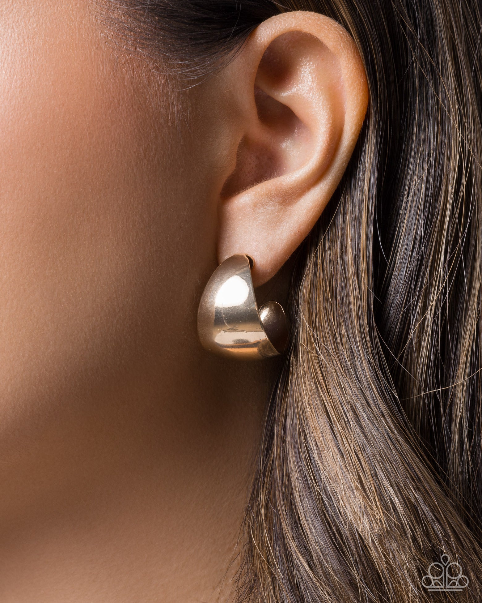 Gold earring worn on an ear with a blurred background