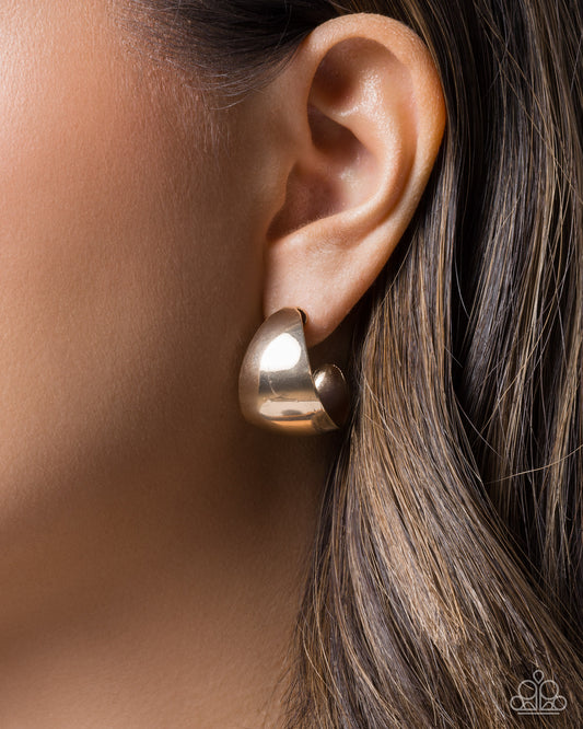 Gold earring worn on an ear with a blurred background