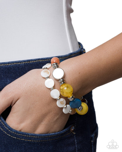 A close-up of a person's wrist wearing two beaded stretch bracelets. One bracelet features white disc beads with silver-toned spacers, and the other features yellow, blue, and orange beads with silver-toned spacers.