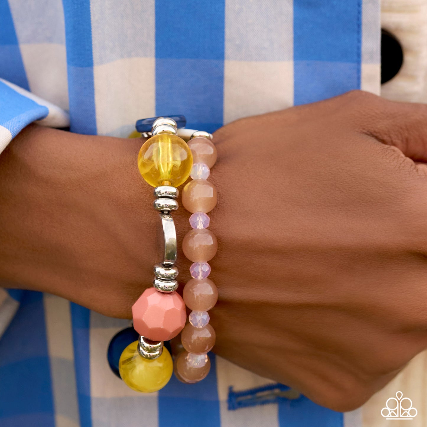 A close-up of a person's wrist wearing two beaded bracelets. One bracelet features translucent yellow beads, a faceted pink bead, and silver-toned spacer beads, while the other features pale pink and lavender beads.