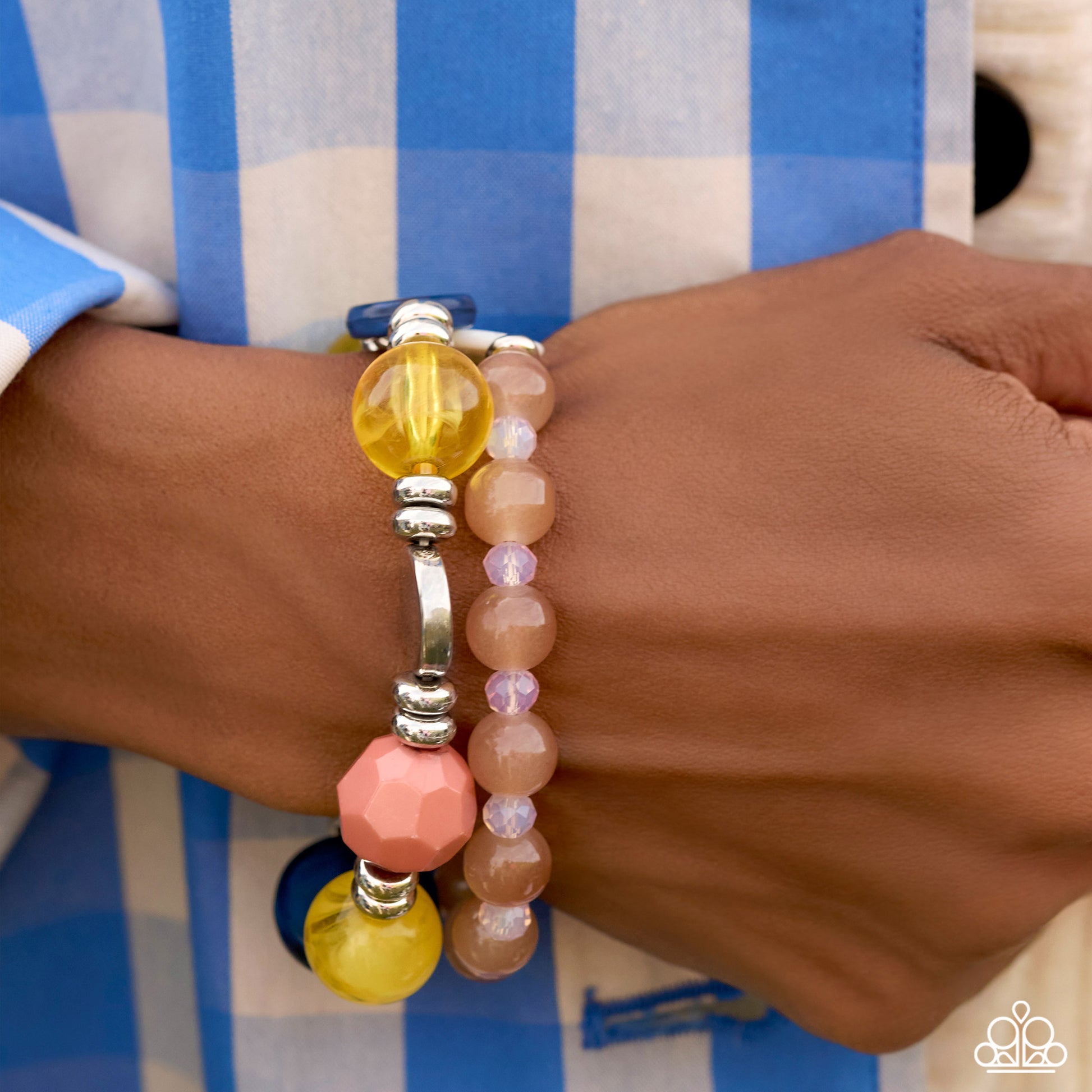A close-up of a person's wrist wearing two beaded bracelets. One bracelet features translucent yellow beads, a faceted pink bead, and silver-toned spacer beads, while the other features pale pink and lavender beads.