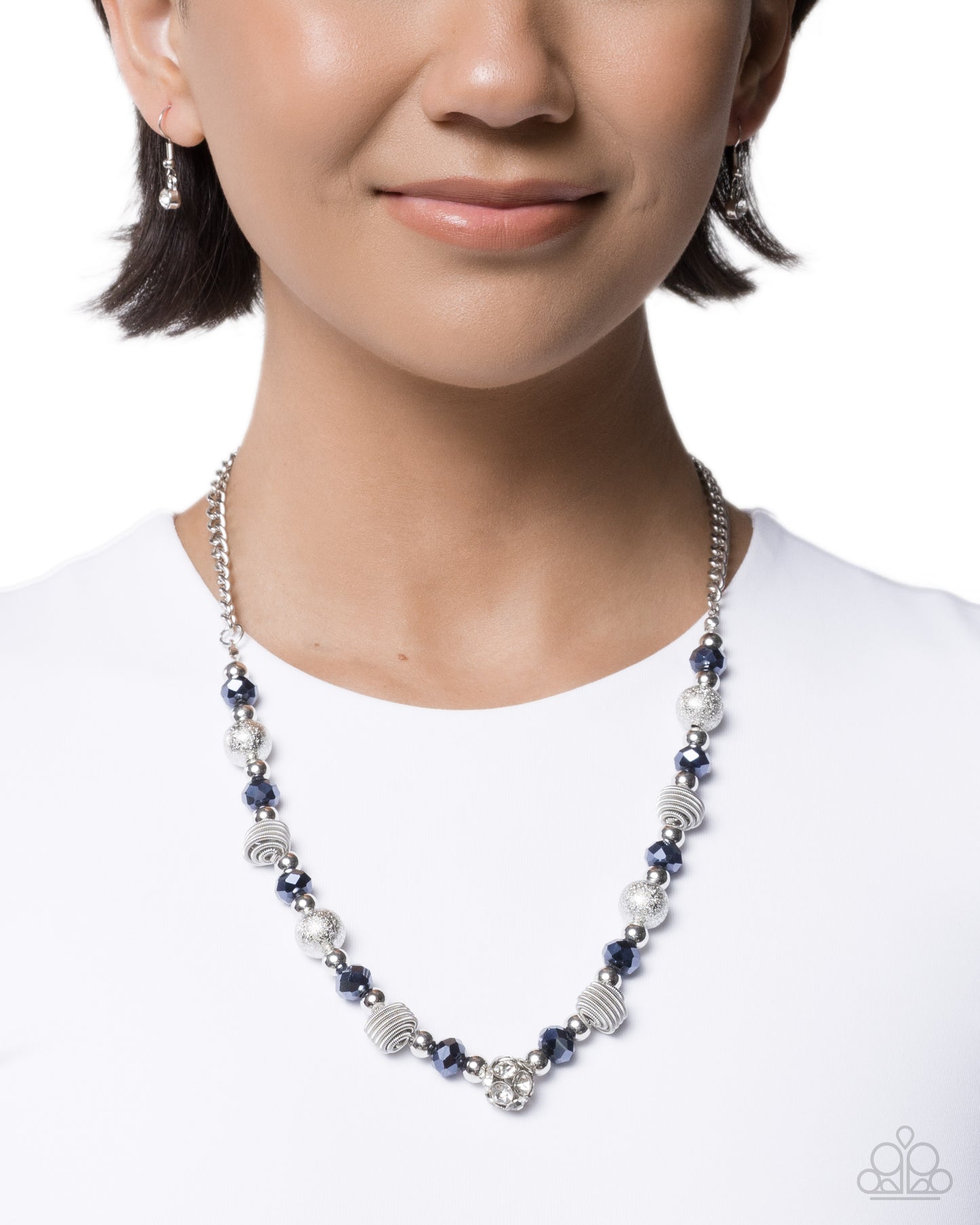 A close-up of a model wearing a silver beaded necklace with navy blue beads and textured silver accents, paired with matching silver drop earrings.