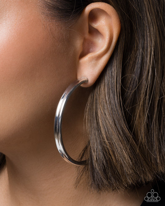 Silver hoop earring worn by a person with brown hair.