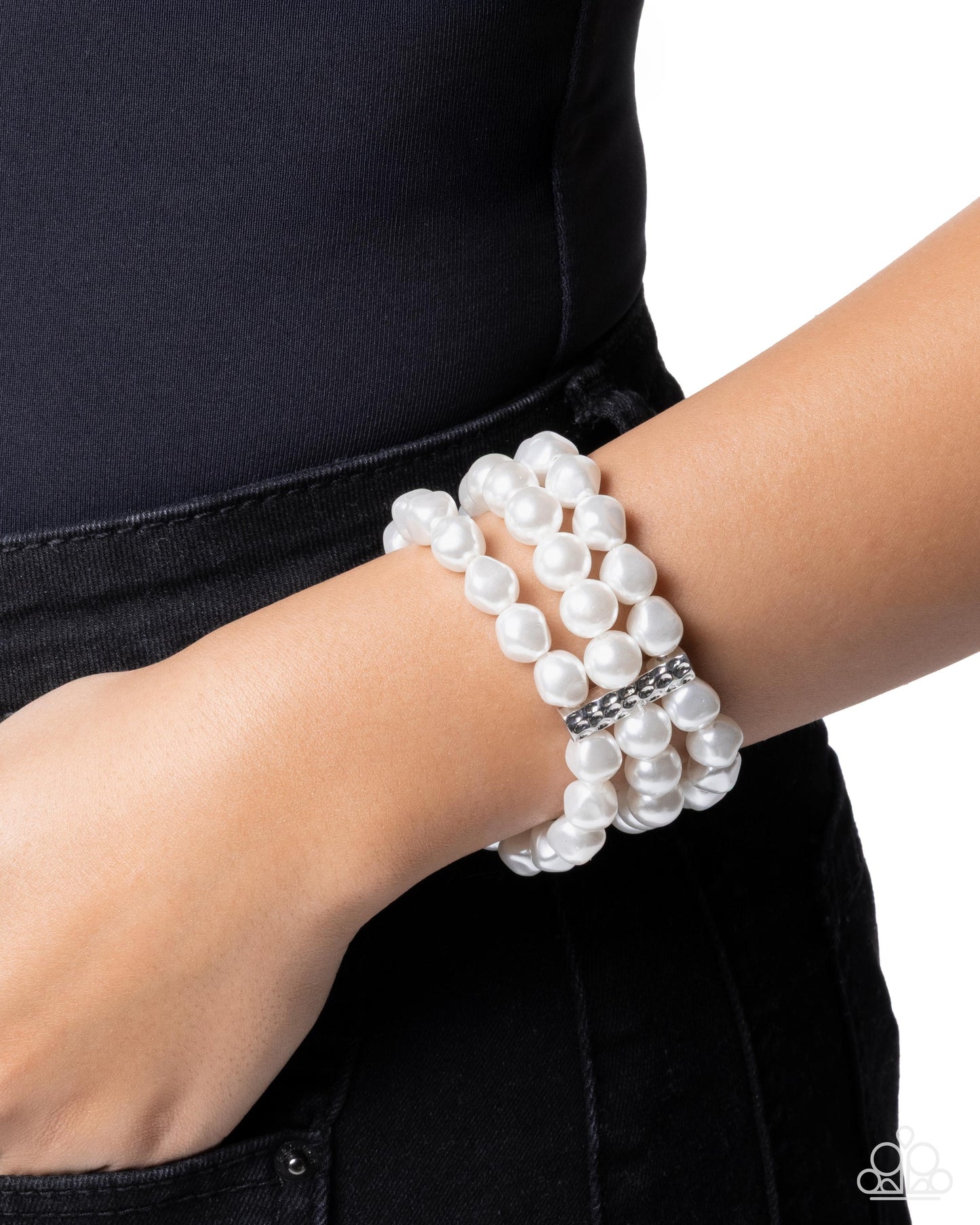 White pearl bracelet on a wrist with a black background