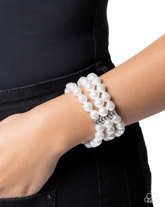 White pearl bracelet on a wrist with a black background