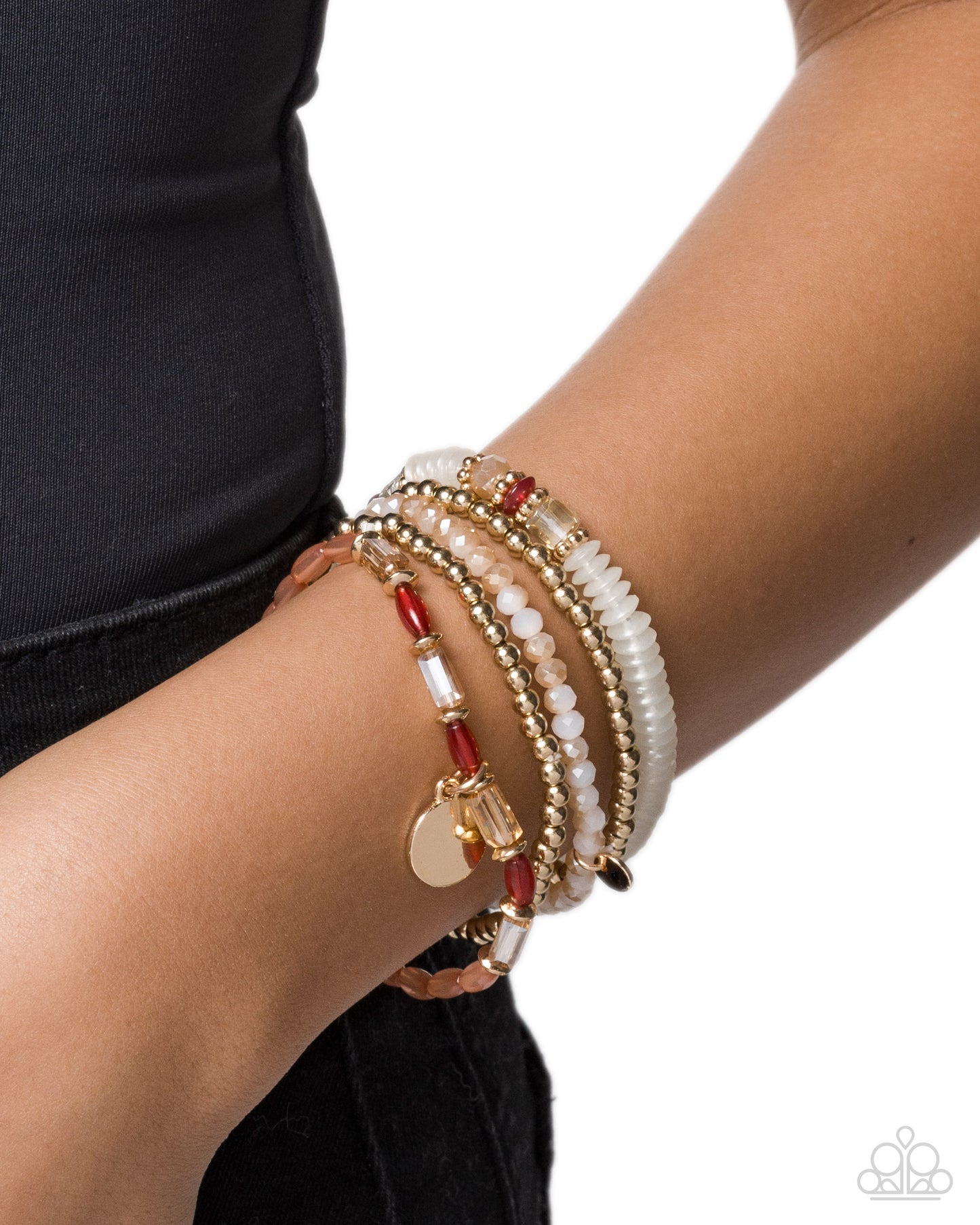 A close-up of a person's wrist wearing a stack of bohemian-style beaded bracelets. The bracelets feature white faux pearls, gold-toned beads, red beads, and a small gold heart charm, set against a clean white background.