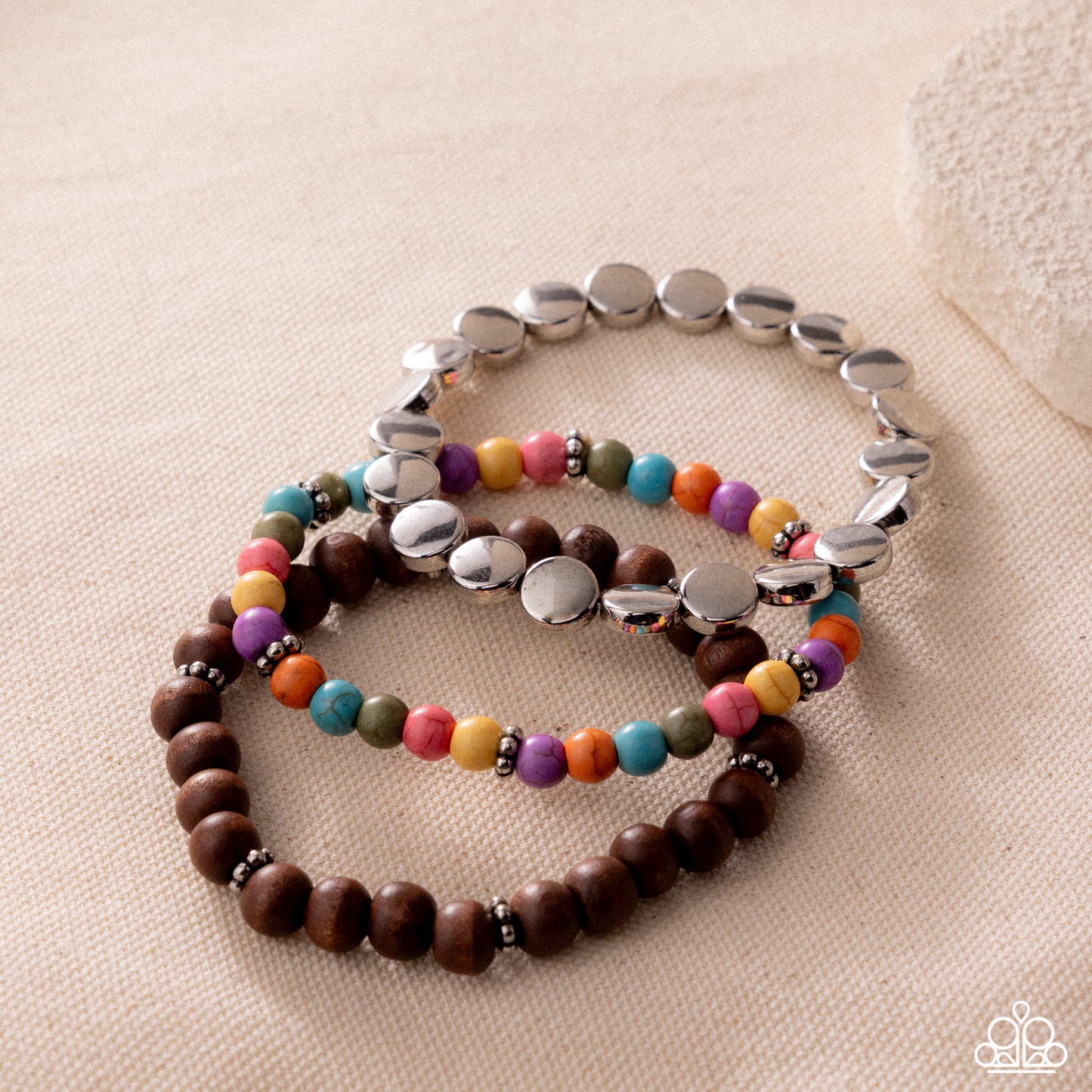 Two bracelets, one with colorful beads and the other with silver beads, on a beige surface.