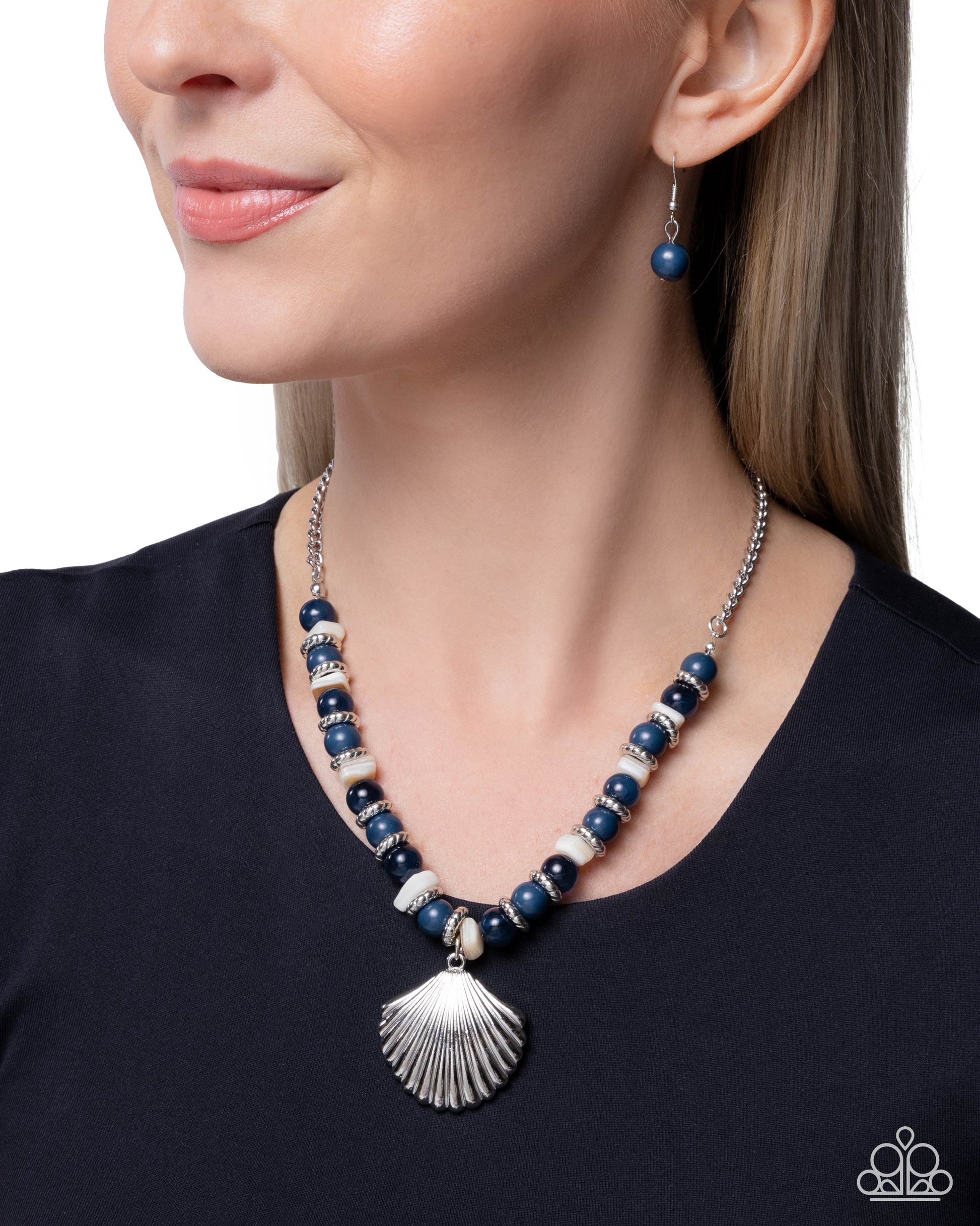 Woman wearing a blue beaded necklace with a shell pendant on a plain background