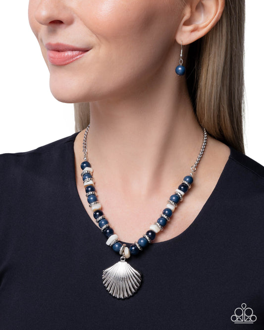 Woman wearing a blue beaded necklace with a shell pendant on a plain background