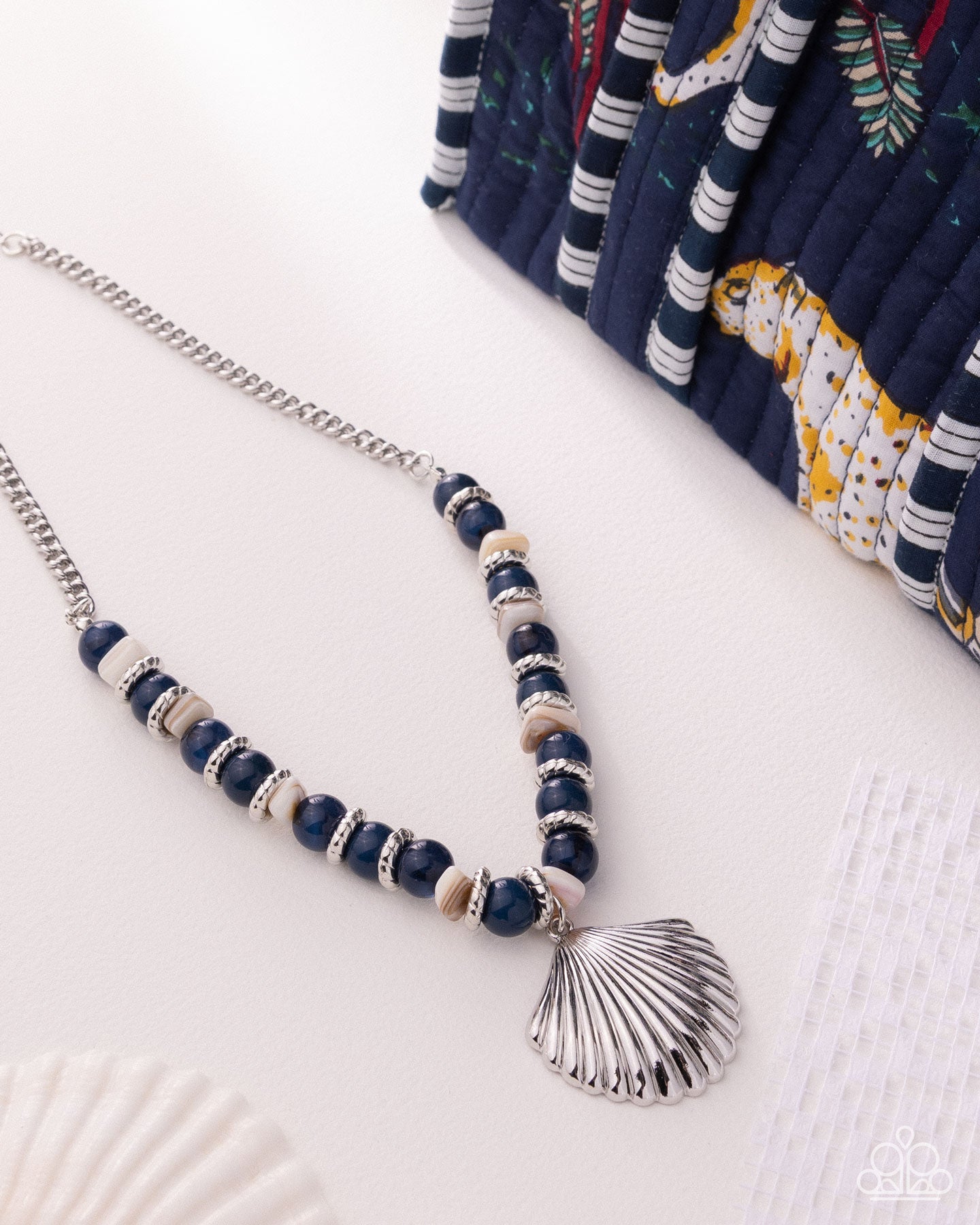 Necklace with blue beads and a shell pendant on a white surface