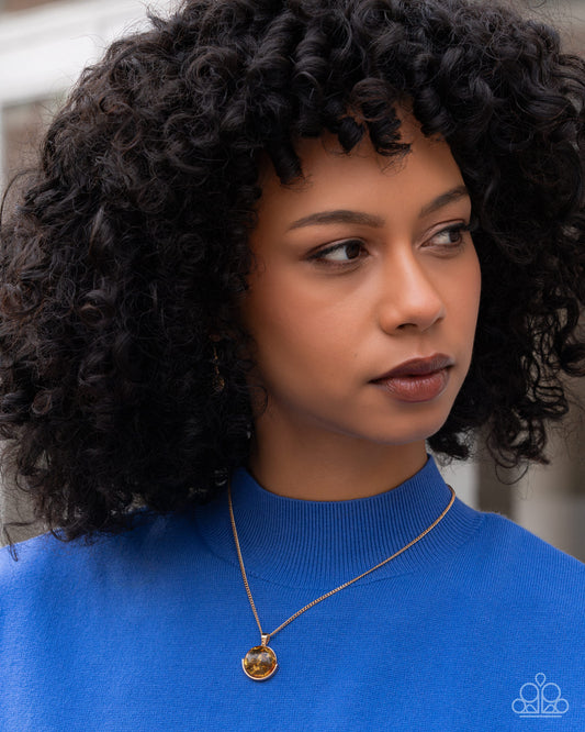 Woman with curly hair wearing a blue sweater and gold necklace.