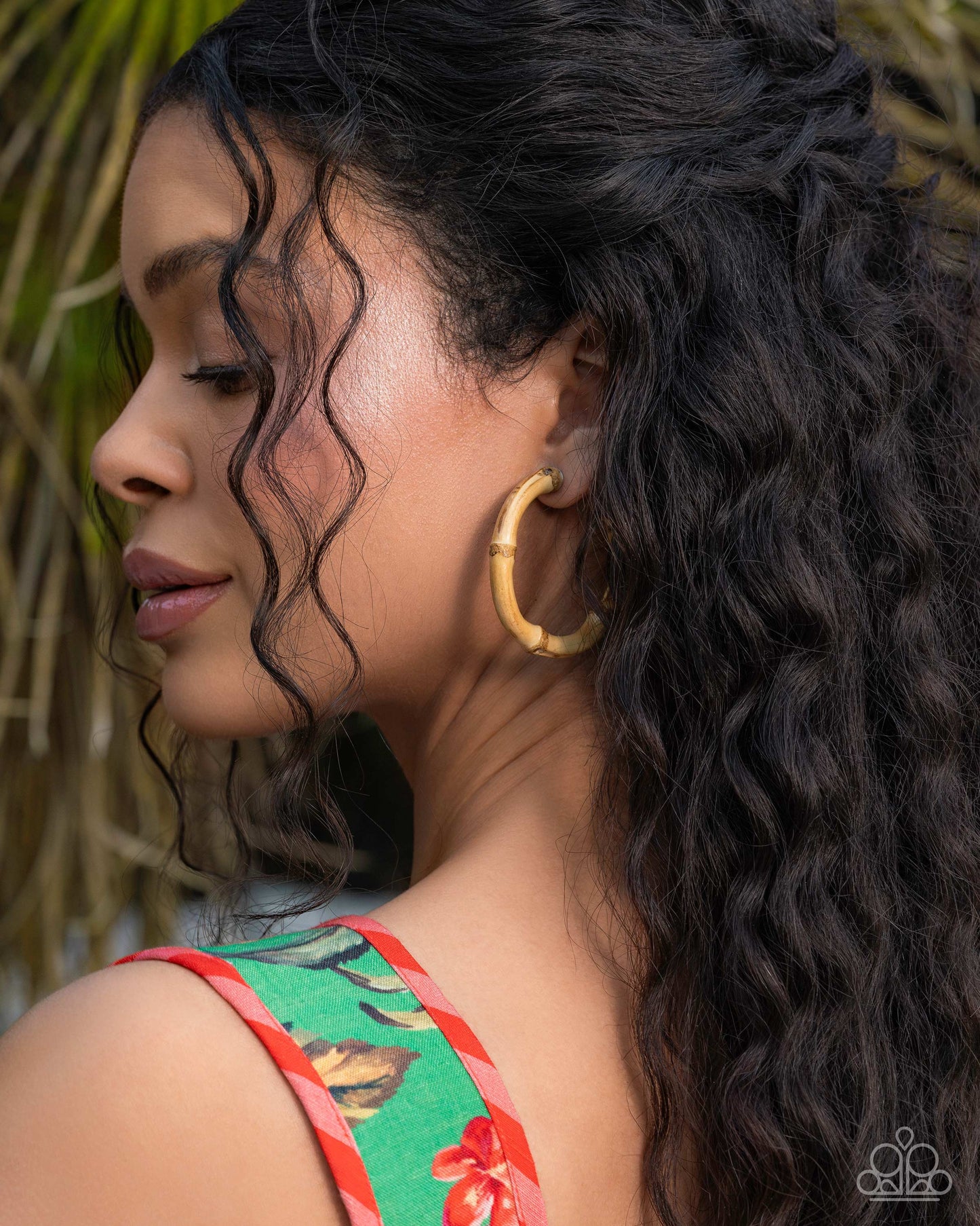Woman with long, wavy hair wearing gold hoop earrings, with a blurred natural background