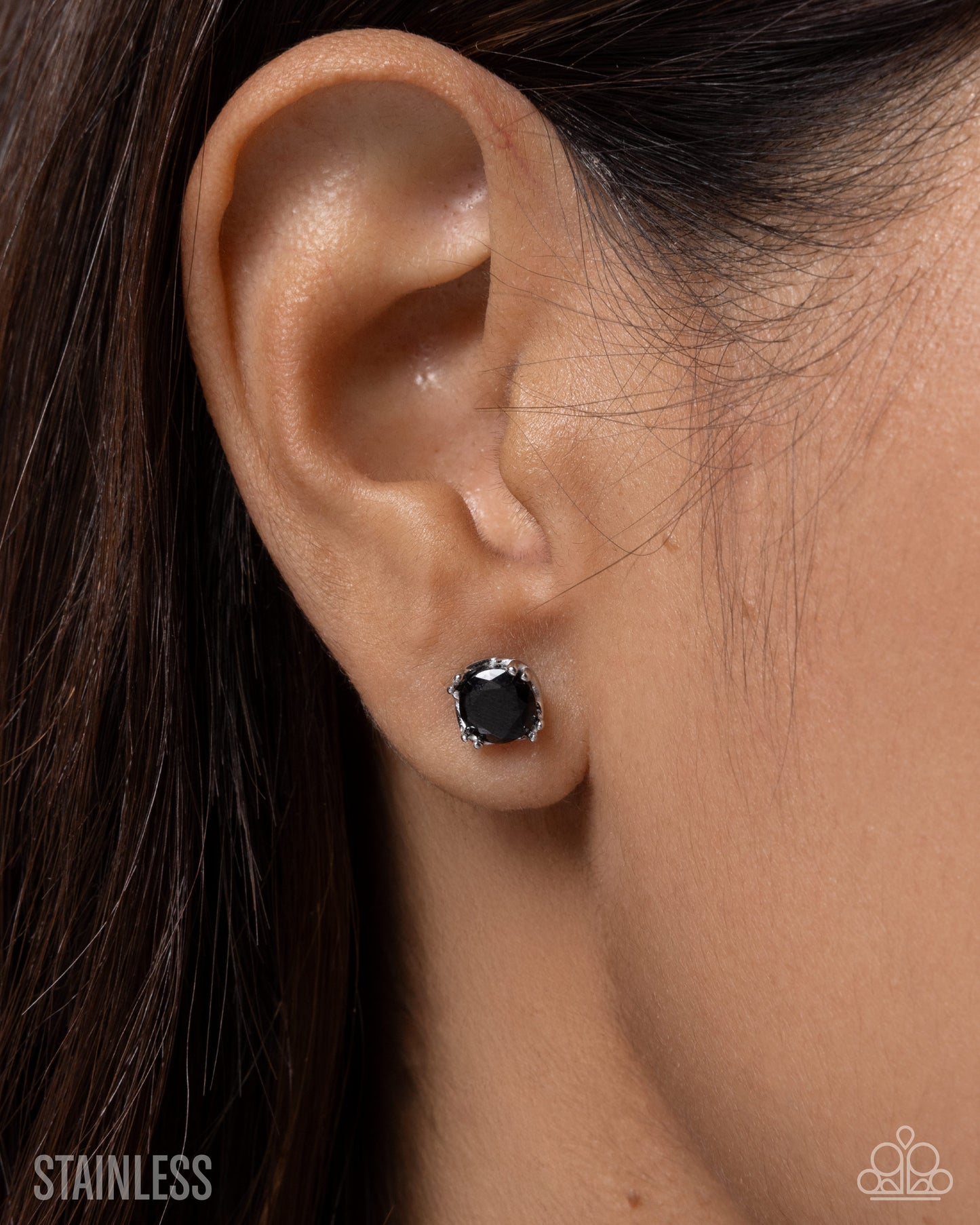 Close-up of an ear wearing a black stud earring with 'Stainless' text below.