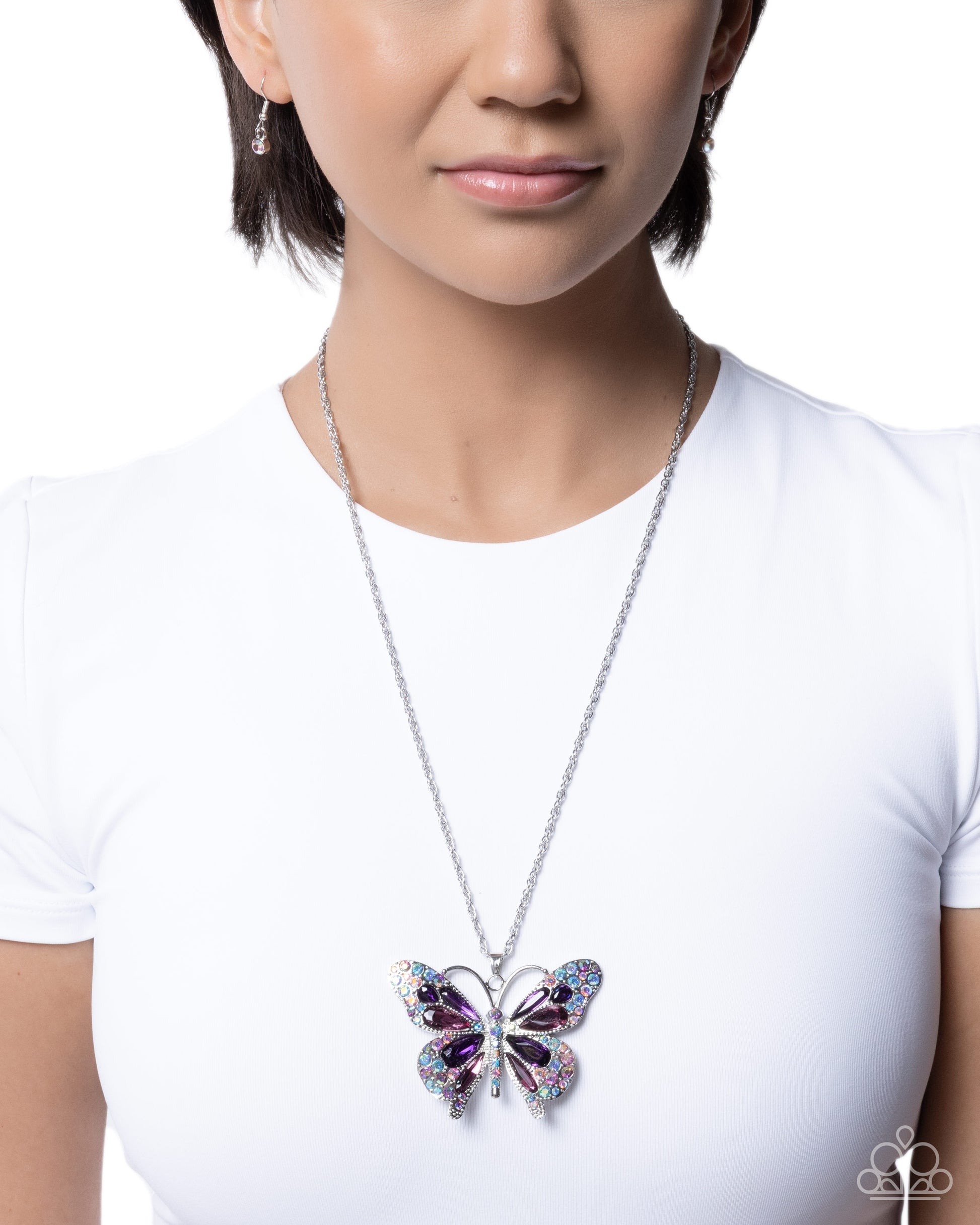 Person wearing a white shirt with a colorful butterfly pendant necklace.