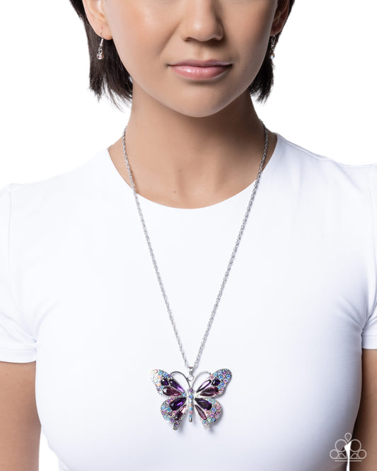 Person wearing a white shirt with a colorful butterfly pendant necklace.