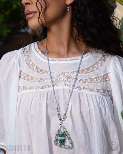 Woman wearing a white blouse with lace details and a long necklace with a green pendant.
