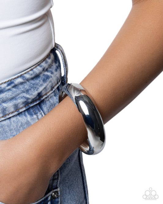 Person wearing a shiny silver bracelet on a plain background