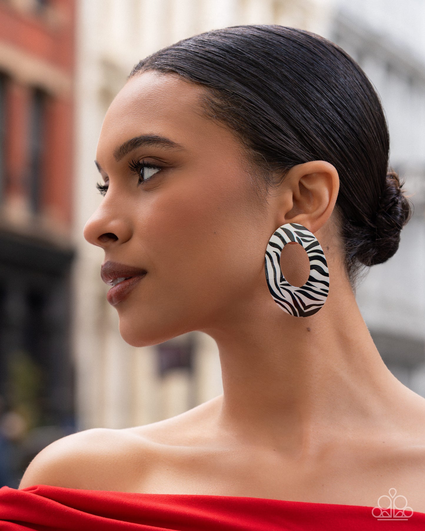 Woman wearing zebra print hoop earrings with a blurred city street background