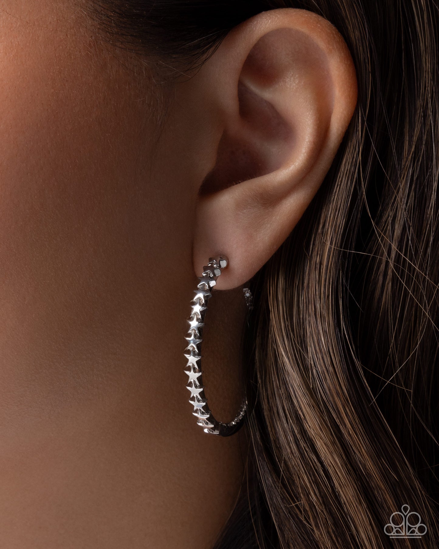 Silver hoop earrings with star details worn by a person with brown hair.