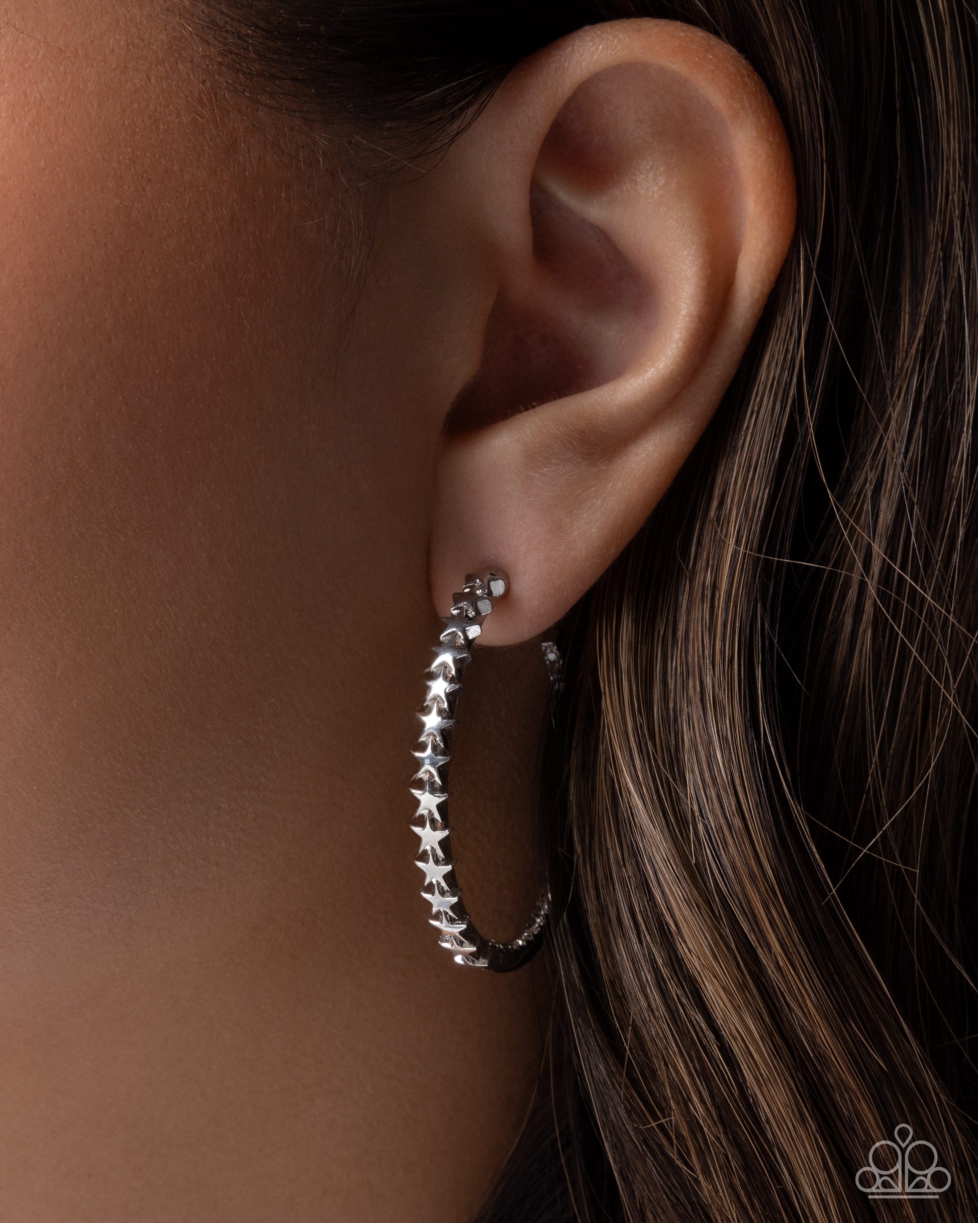 Silver hoop earrings with star details worn by a person with brown hair.