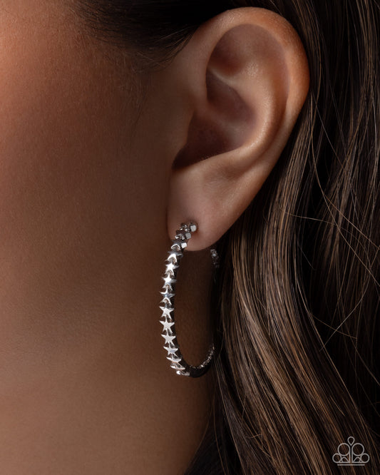 Silver hoop earrings with star details worn by a person with brown hair.