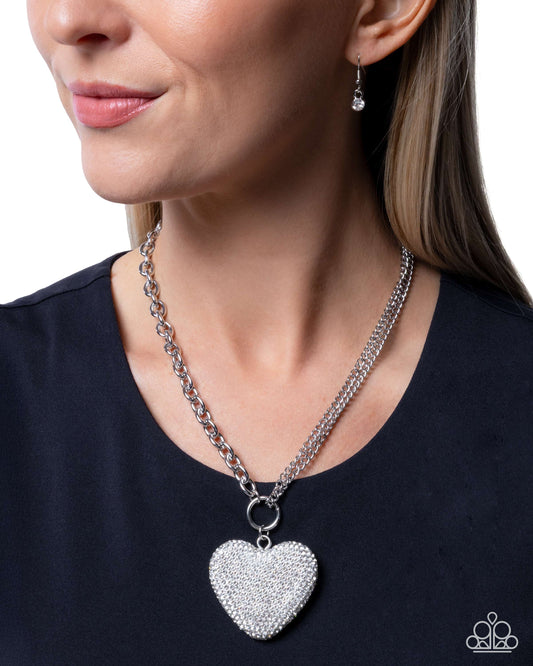 Woman wearing a silver heart-shaped pendant necklace and matching earrings.