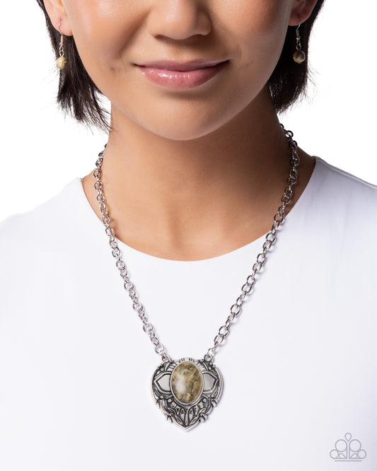 Person wearing a silver chain necklace with a heart-shaped pendant on a white background