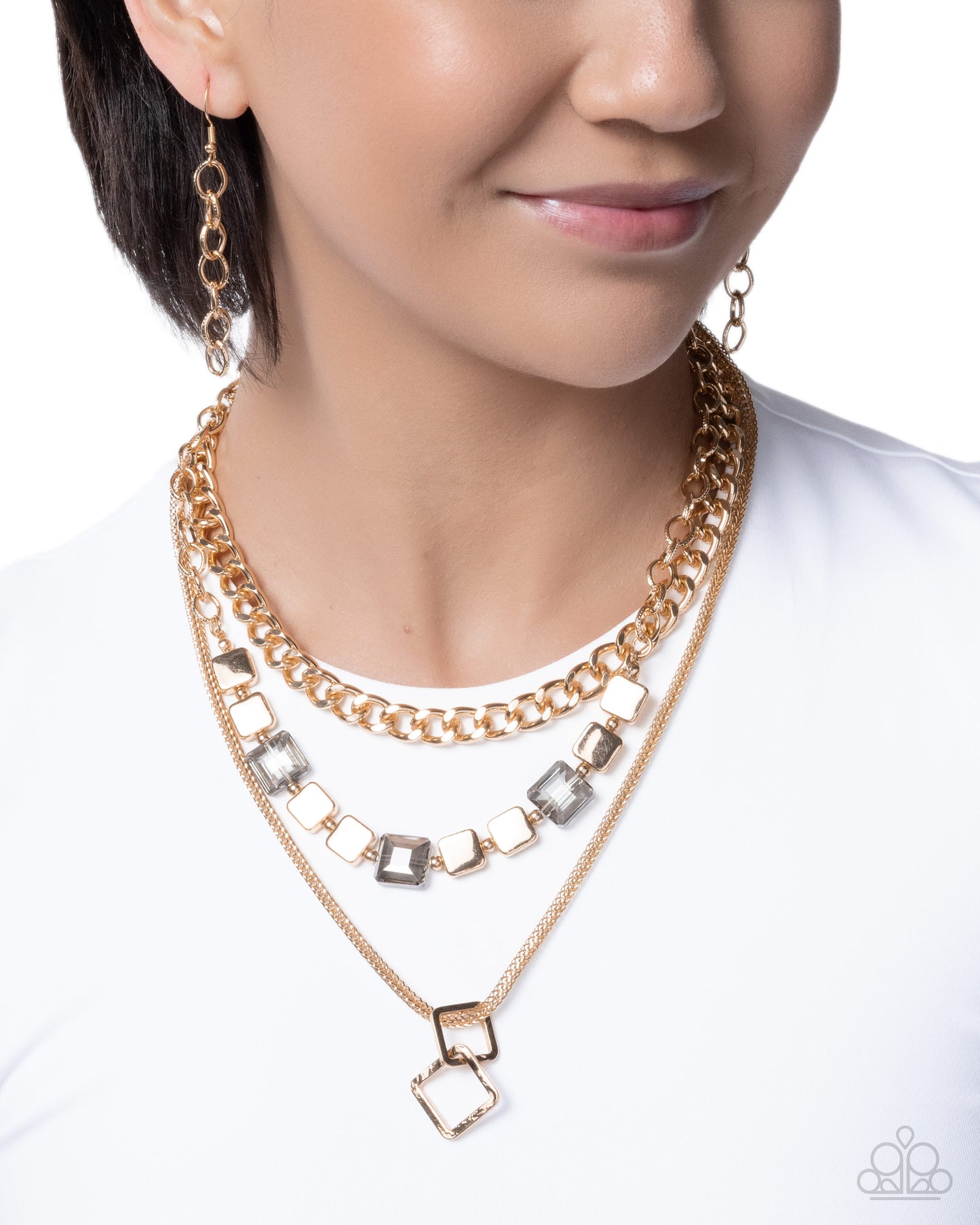 A close-up of a woman wearing a layered gold necklace set with square-cut clear rhinestones and matching drop earrings, against a white background.