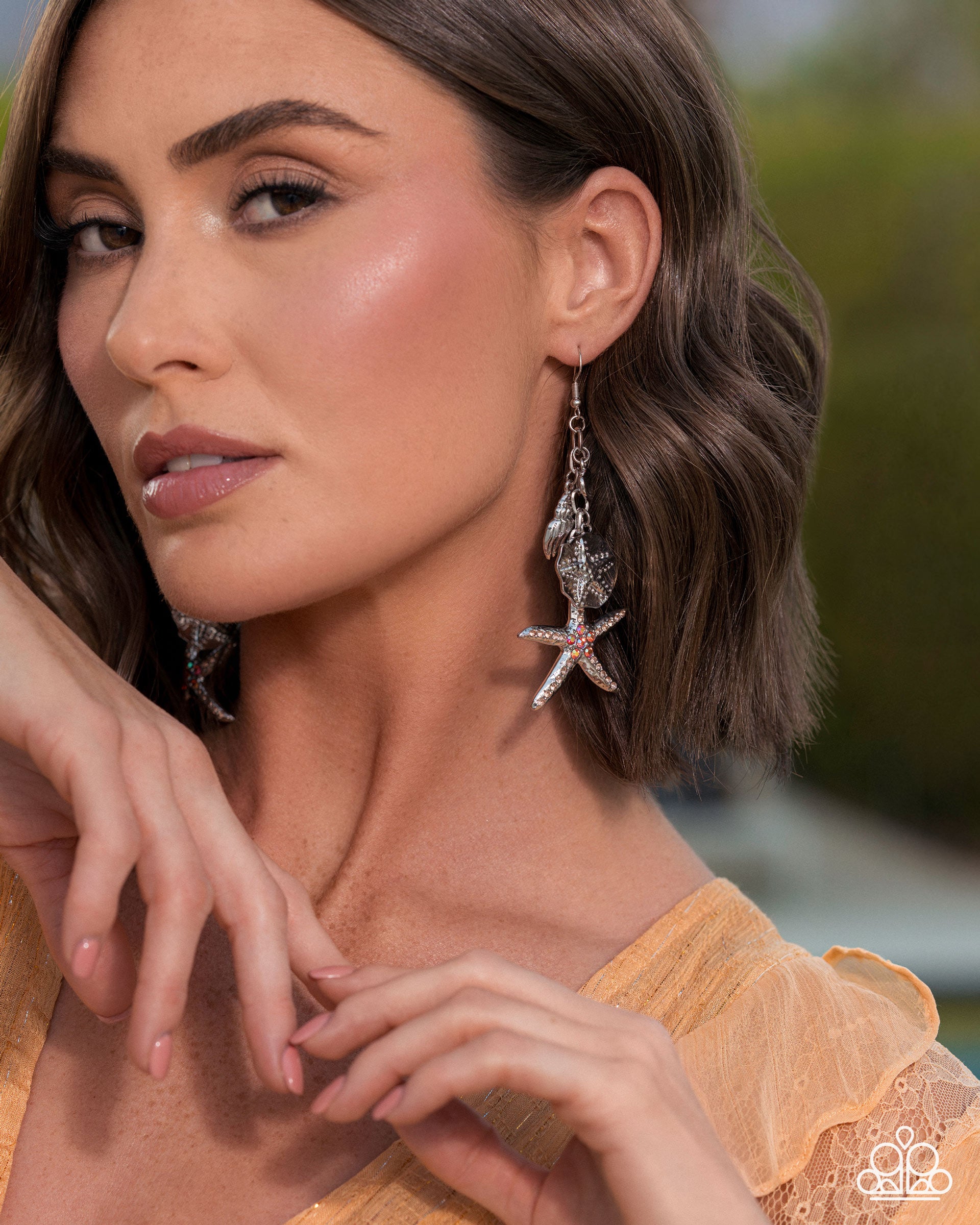 Woman wearing starfish earrings with a blurred outdoor background