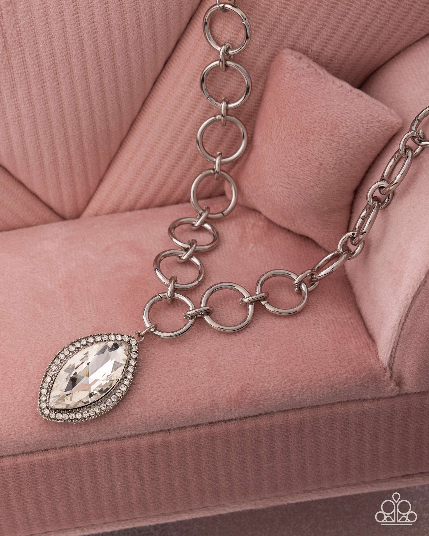 Silver chain bracelet with a teardrop-shaped crystal charm on a pink textured surface