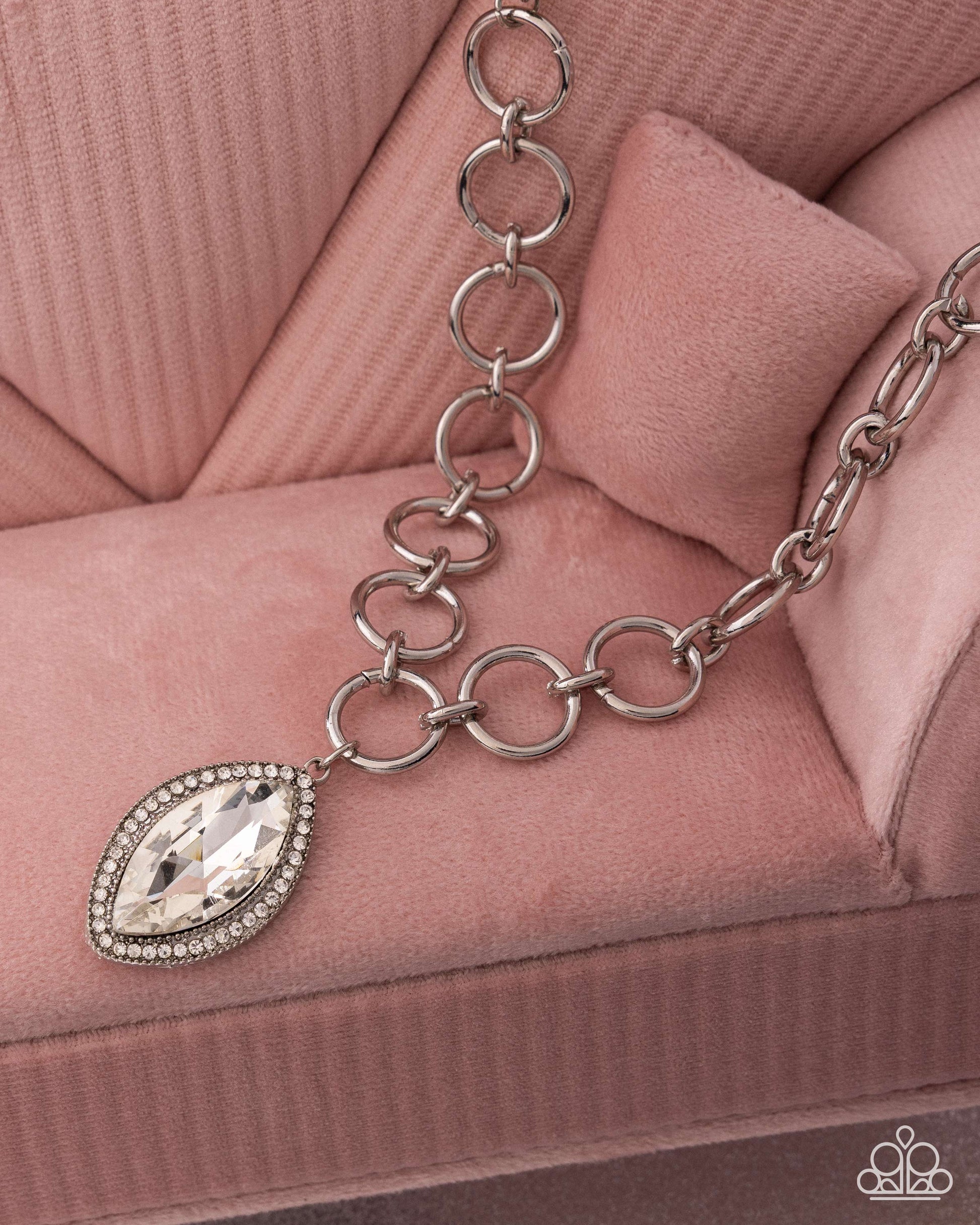 Silver chain bracelet with a teardrop-shaped crystal charm on a pink textured surface