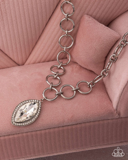 Silver chain bracelet with a teardrop-shaped crystal charm on a pink textured surface