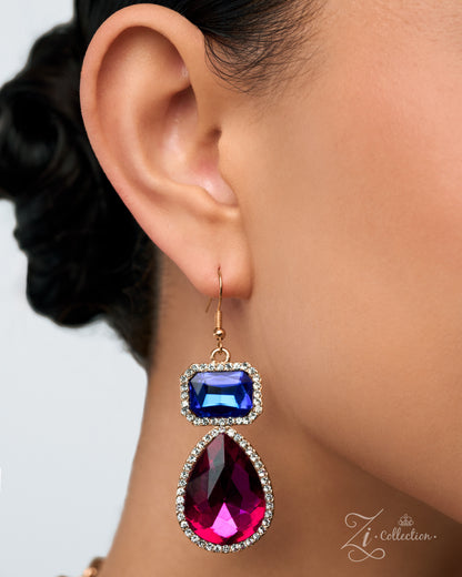 A close-up of a model's ear wearing a gold drop earring with a rectangular blue gemstone and a larger teardrop-shaped magenta pink gemstone, both accented with small clear rhinestones.