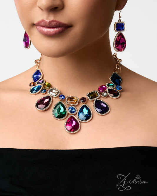 A close-up of a model wearing a gold-plated statement necklace and matching drop earrings with large, colorful teardrop and oval rhinestones in shades of pink, blue, green, and purple, set against a clean white background.